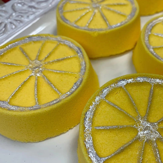 Yellow lemon-shaped bath bombs with silver detailing on a white plate