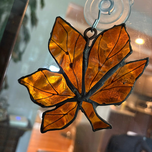 Stained glass leaf decoration on a suction cup against a blurred indoor background