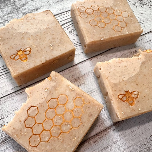 Four square bars of soap with honeycomb and bee designs on a wooden surface