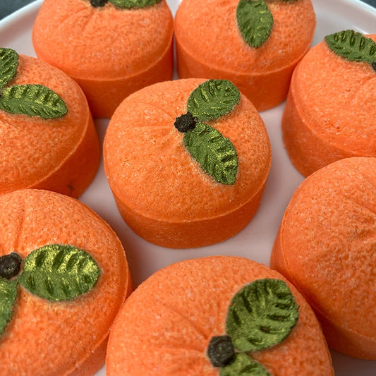 Orange bath bombs shaped like citrus with green leaves on a white plate.